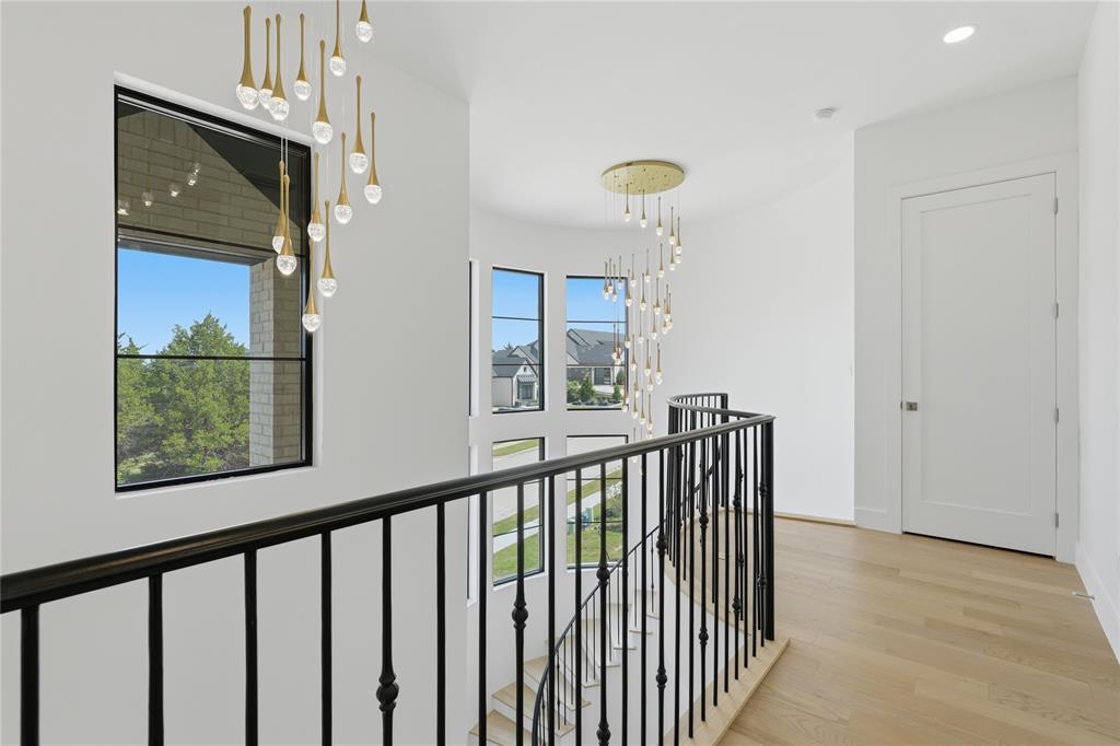 Upper-level landing featuring light wood-finish flooring, white walls, and a black wrought-iron railing