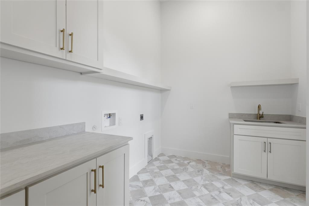Utility room featuring checkerboard tile flooring, white cabinetry with gold-toned hardware, light-toned countertops, and a utility sink with a brass-finish faucet