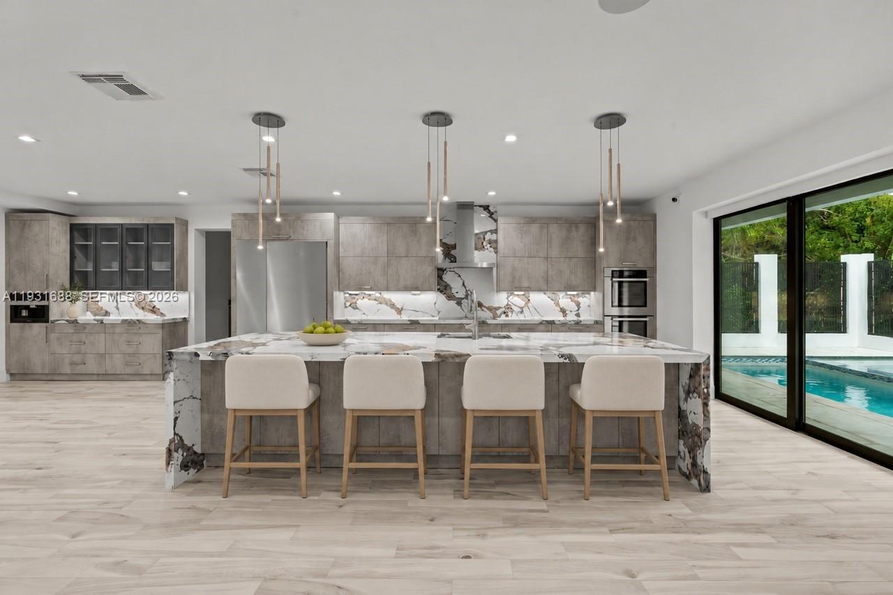 Chef's kitchen featuring flat-panel cabinetry, a waterfall island with stone countertop, built-in stainless steel appliances, and multi-light pendant fixtures