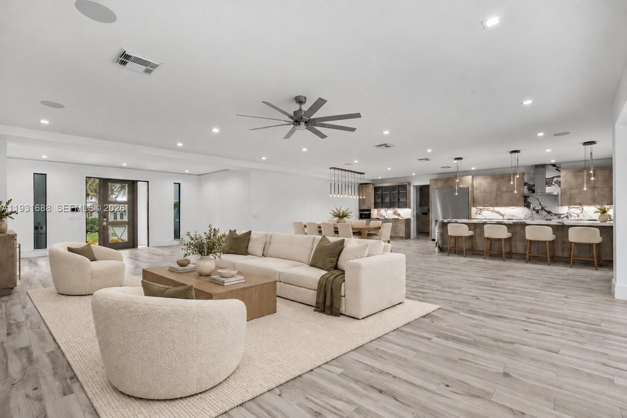 Open-concept interior featuring wood-finish flooring, recessed lighting, a modern ceiling fan, and a kitchen island with stone-finish countertops and backsplash