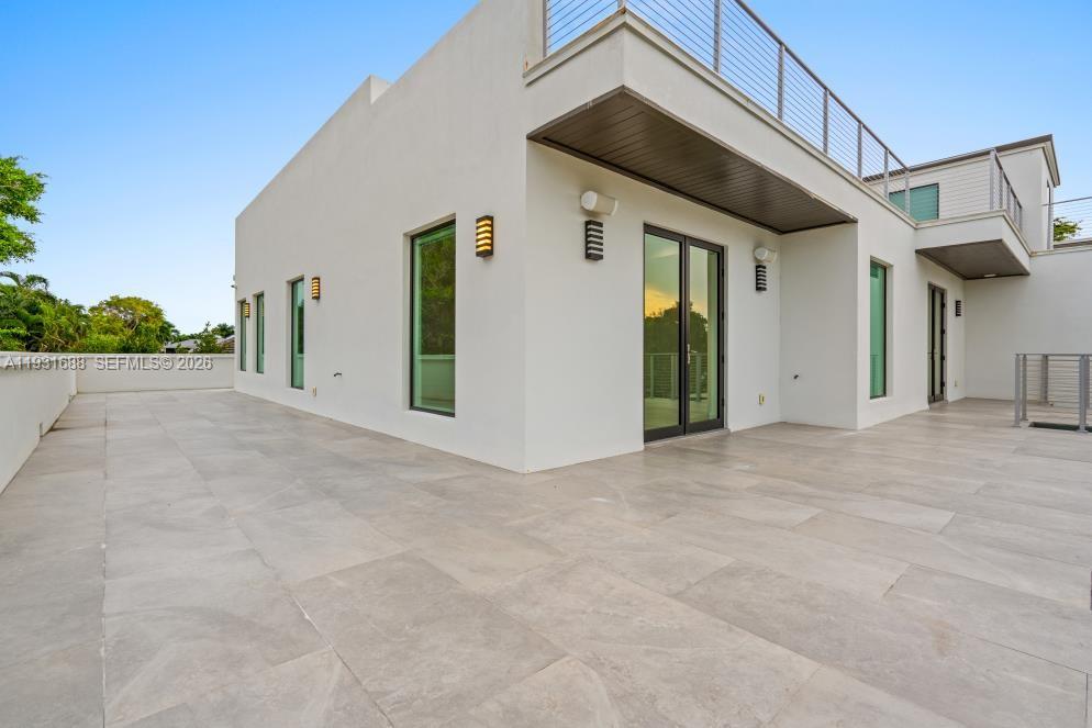 Expansive rooftop terrace featuring stone-tile flooring, perimeter walls, metal cable railings, and exterior wall-mounted lighting