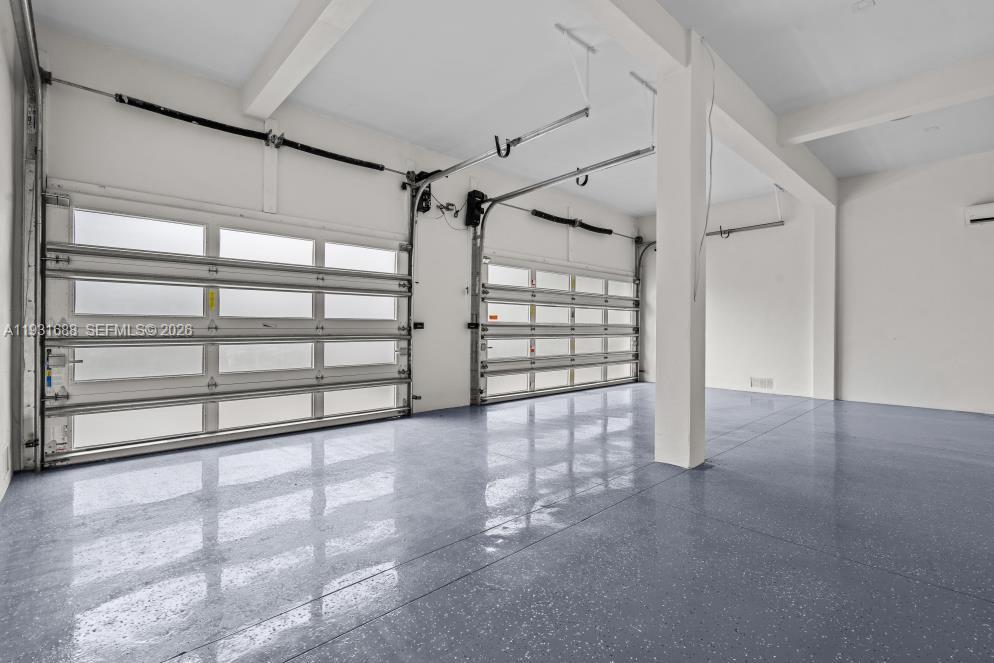 Multi-car garage featuring epoxy-coated flooring, white-finished walls, exposed structural beams, and two overhead metal doors with frosted glass inserts