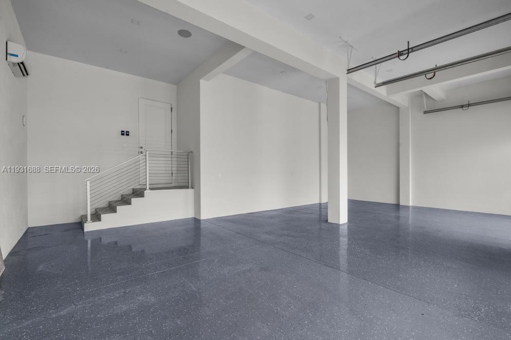 Open-concept interior featuring high ceilings, epoxy-finished flooring, structural support columns, and an elevated staircase with horizontal cable railing