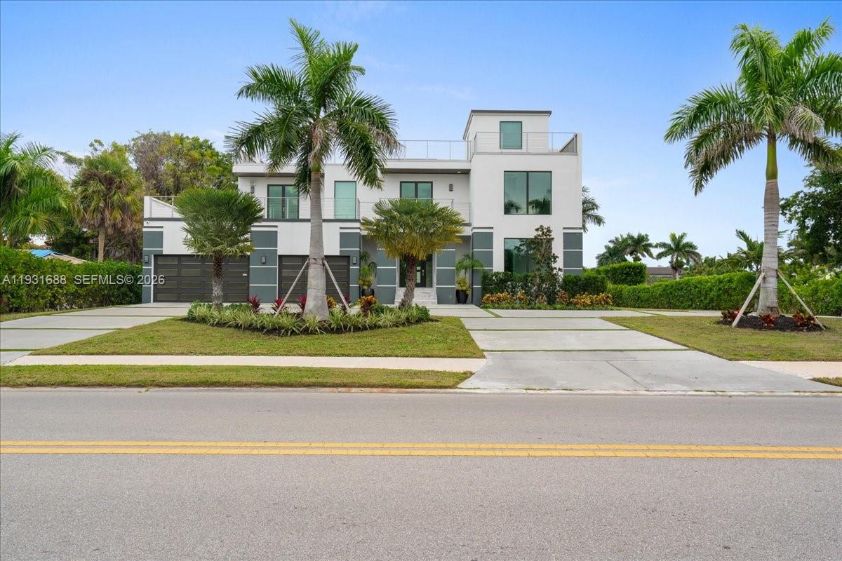Modern two-story exterior featuring multi-level balconies, expansive multi-pane windows, a split three-car garage, and a concrete paver driveway
