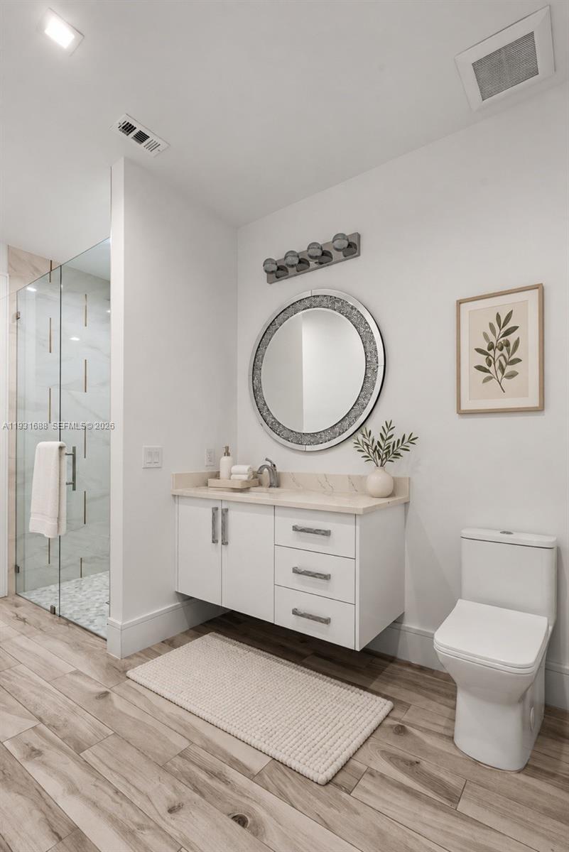 Floating vanity featuring a solid surface countertop, rectangular under-mount sink, and contemporary hardware, complemented by a glass-enclosed shower with tiled flooring and wood-finish flooring throughout