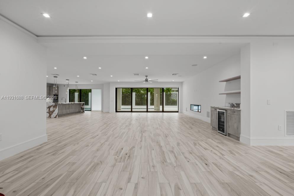 Open-concept interior featuring wood-finish flooring, recessed lighting, multi-panel sliding glass doors, a built-in beverage center, and a horizontal wall-integrated fireplace