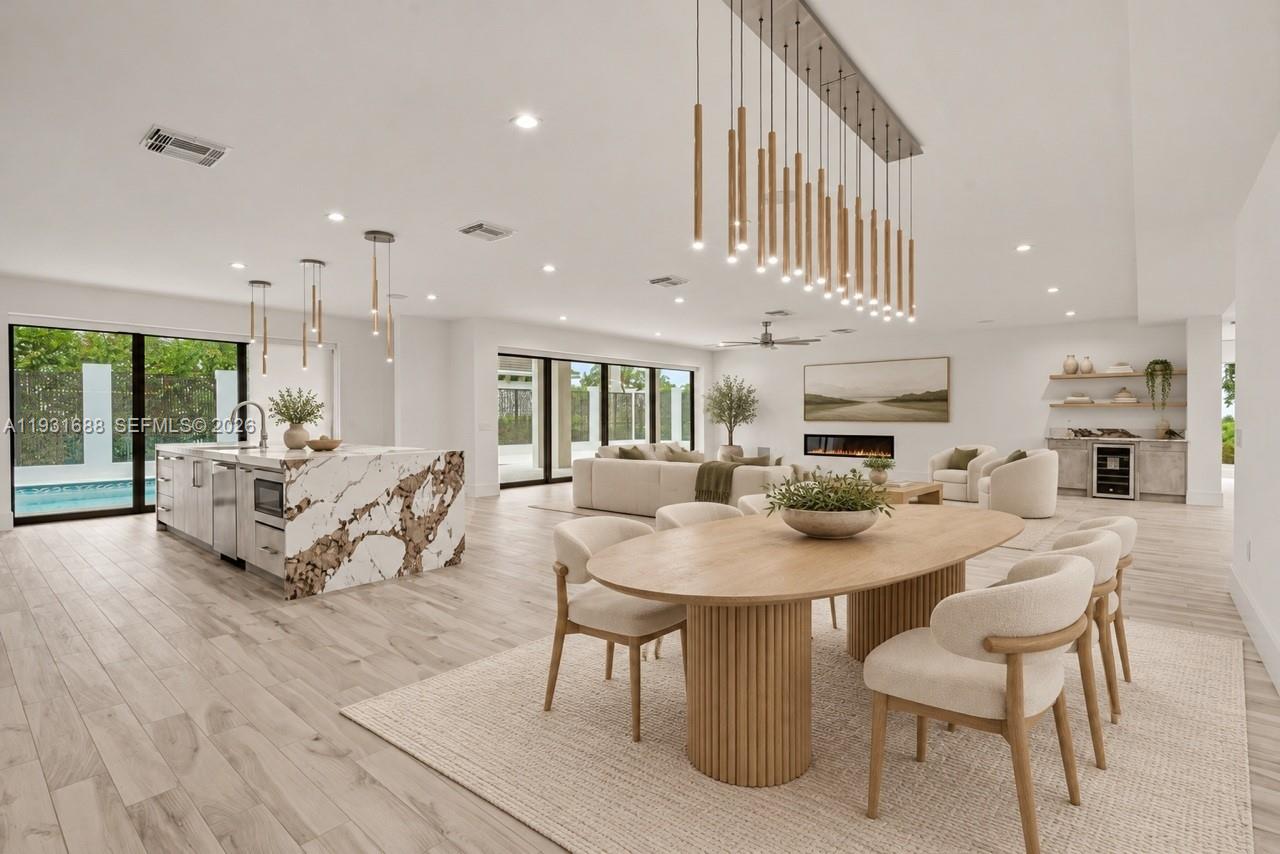 Open-concept interior featuring wood-finish flooring, a kitchen island with stone waterfall edges, floor-to-ceiling sliding glass doors, a linear fireplace, and tiered pendant lighting