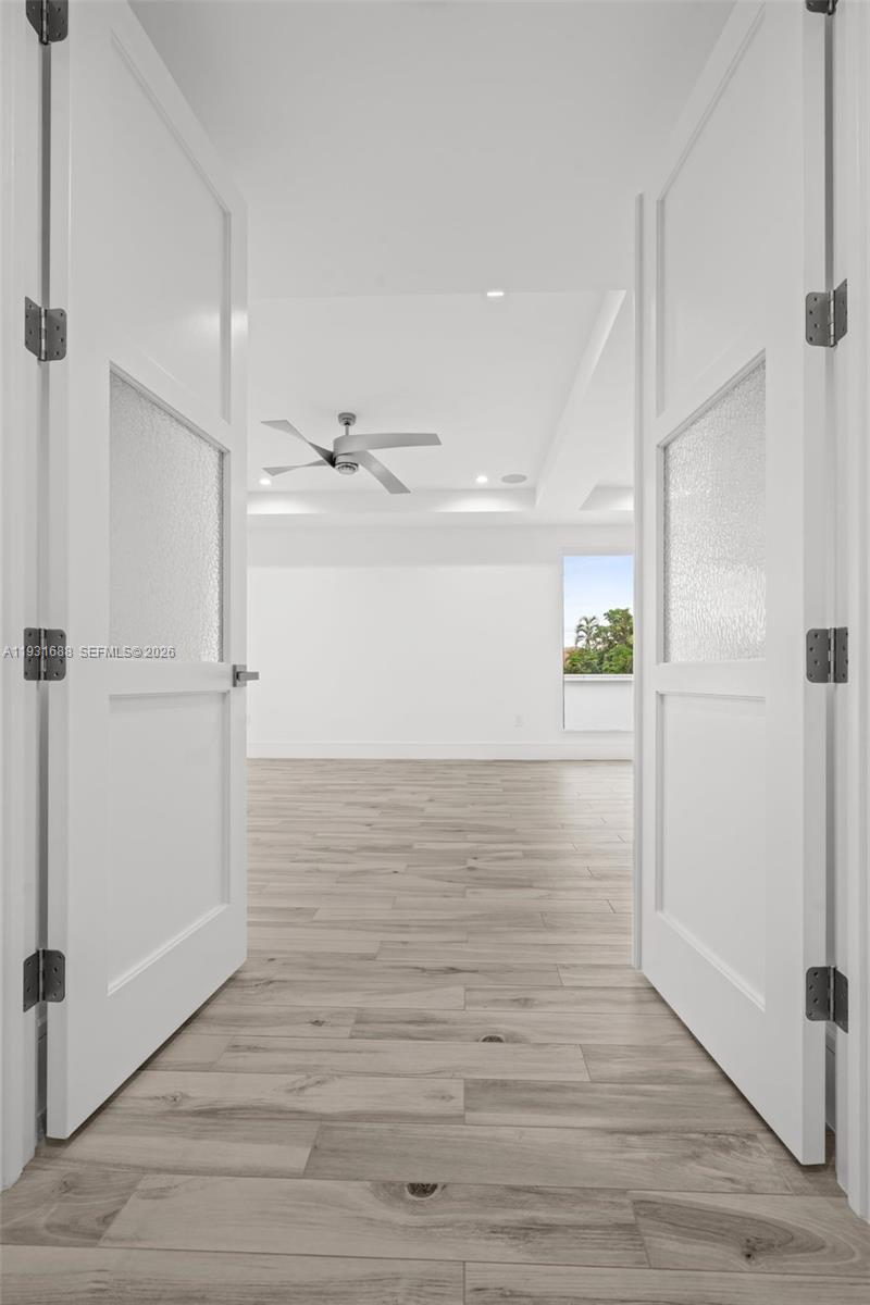 Double doors with frosted glass inserts featuring wood-finish flooring, a tray ceiling, and a ceiling fan