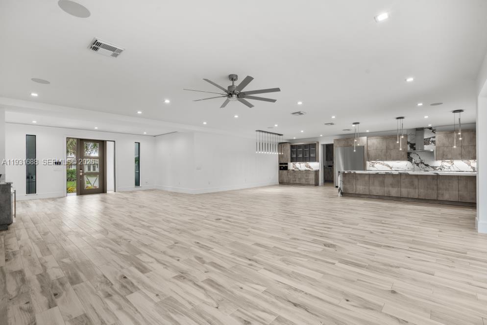 Open-concept interior featuring light wood-finish flooring, recessed lighting, a modern ceiling fan, and a kitchen equipped with stone-patterned backsplashes and integrated cabinetry