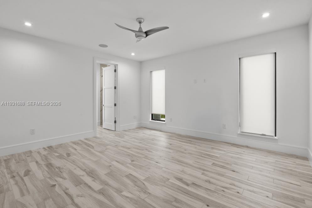 Neutral interior featuring wood-finish flooring, recessed lighting, a modern ceiling fan, and dual windows with roller shades