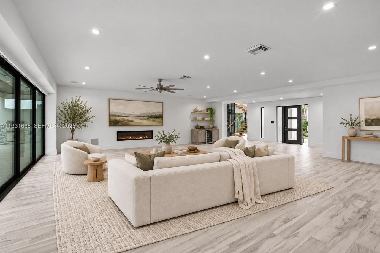 Open-concept room featuring wood-finish flooring, recessed lighting, a linear electric fireplace, sliding glass wall panels, and a built-in refreshment center with shelving