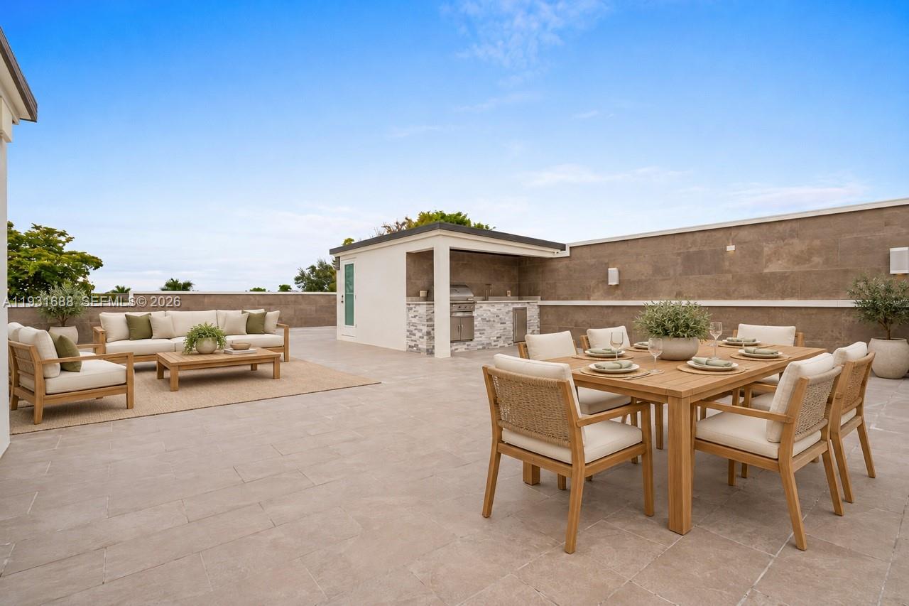 Expansive rooftop terrace featuring large-format tile flooring, a built-in outdoor kitchen with stone veneer cladding, perimeter masonry walls, and wall-mounted exterior lighting