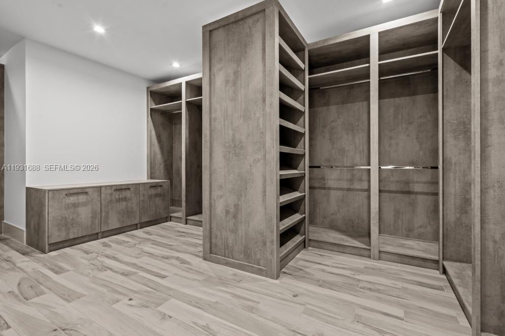 Custom walk-in wardrobe featuring textured wood-finish cabinetry, floor-to-ceiling shelving, integrated hanging rods, low-profile storage drawers, and wood-finish flooring