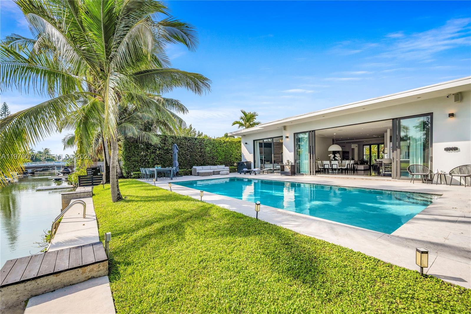 Waterfront backyard featuring a rectangular swimming pool, stone-paver pool deck, manicured lawn, and natural hedge perimeter