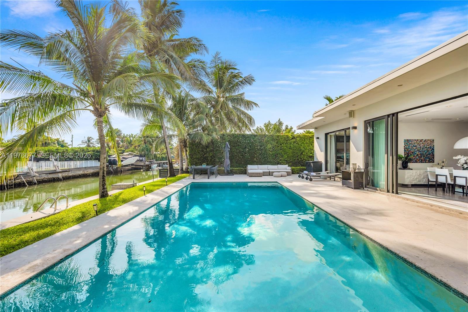In-ground swimming pool with stone-surround. patio, waterfront bulkhead, and privacy-hedged perimeter. Oversize pool