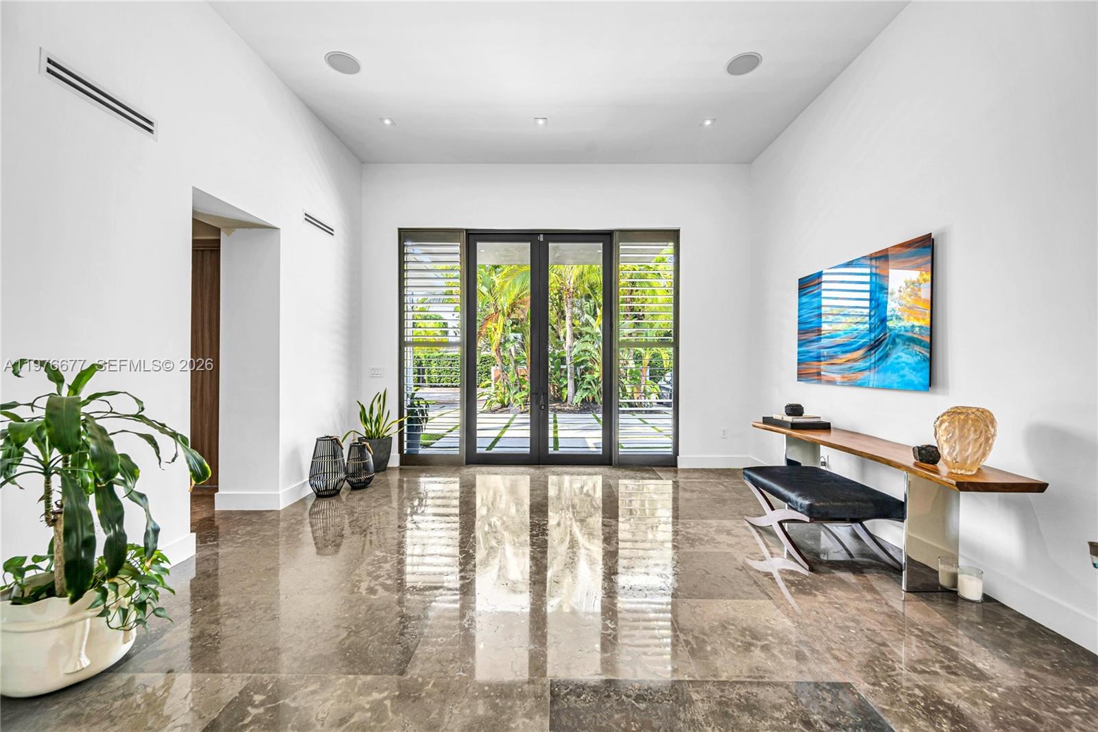 Grand entryway featuring high ceilings, polished stone flooring, recessed lighting, and expansive glass-paned double doors with integrated shutters