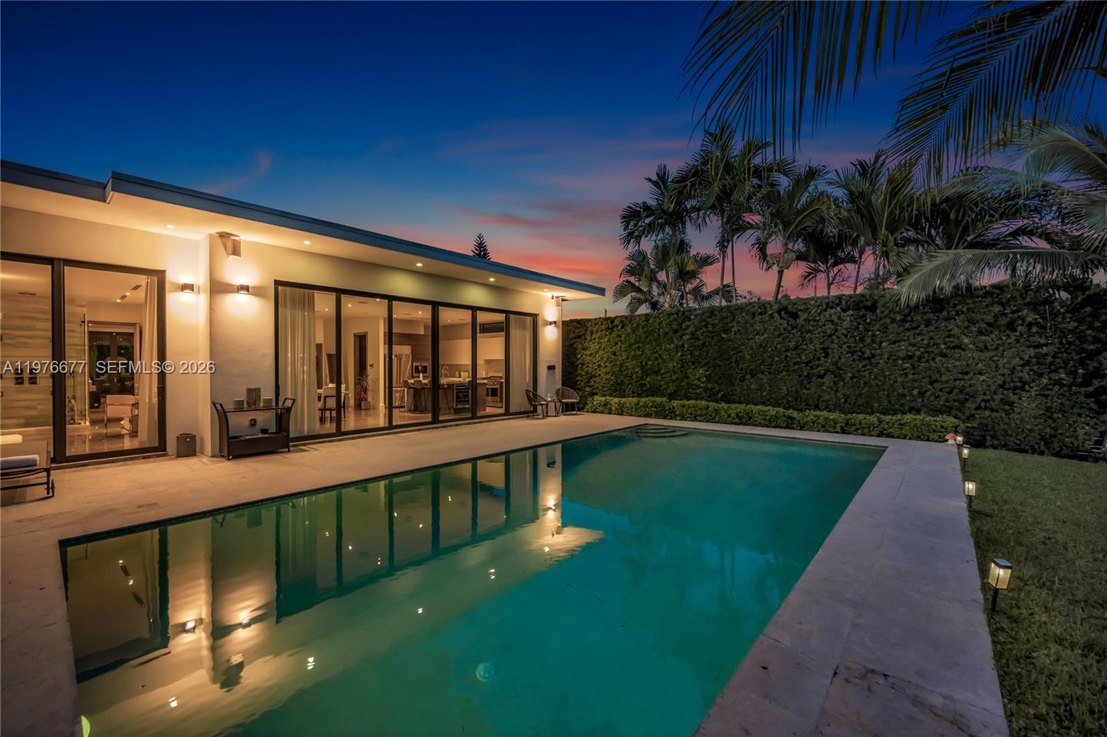 Exterior swimming pool with stone-tile surround, expansive sliding glass walls, and a tall privacy hedge