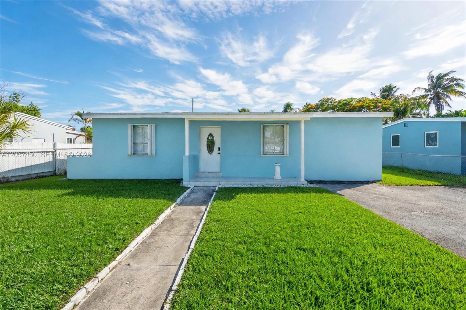 Single-story exterior with light blue siding, white trim accents, a covered front entry, and a paved driveway