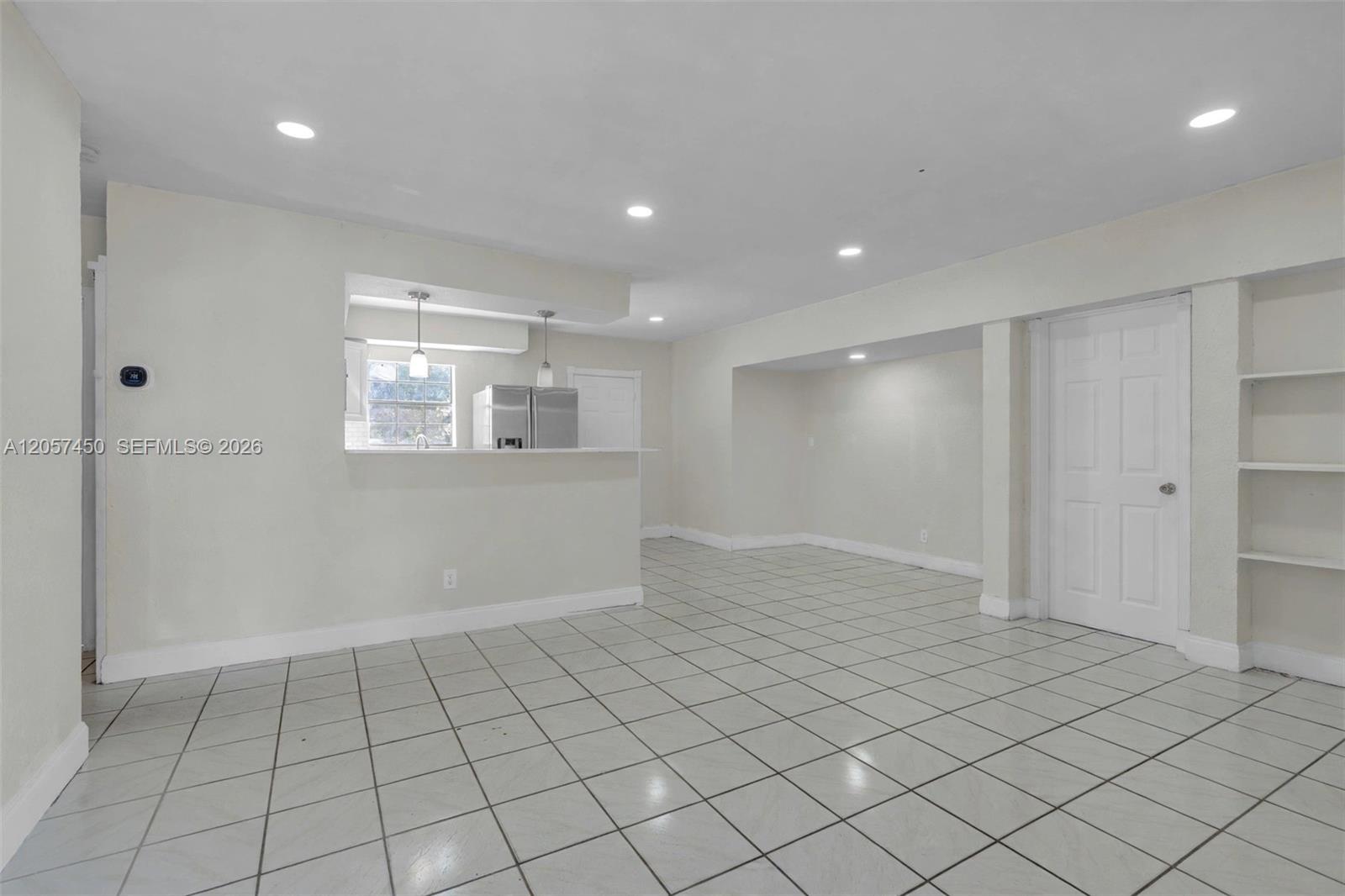 Open interior space featuring light-colored tile flooring, recessed lighting, a built-in shelving unit, and a pass-through opening