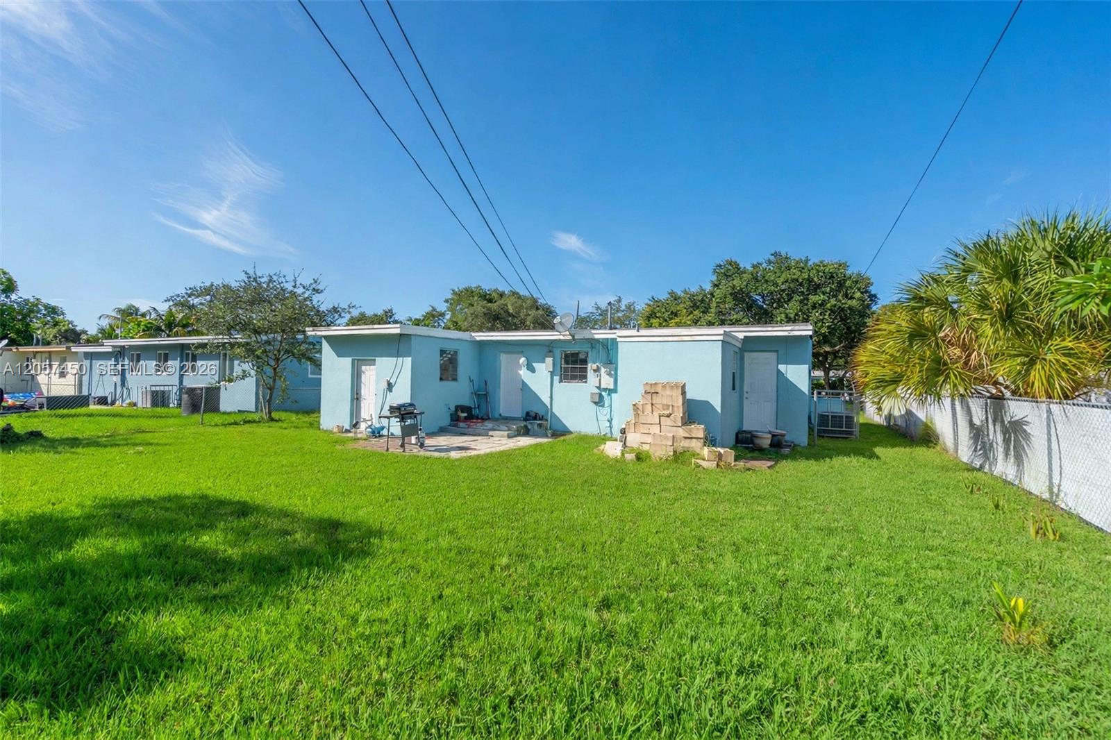 Spacious backyard featuring a grass lawn, paved patio area, chain-link fencing, and mature trees