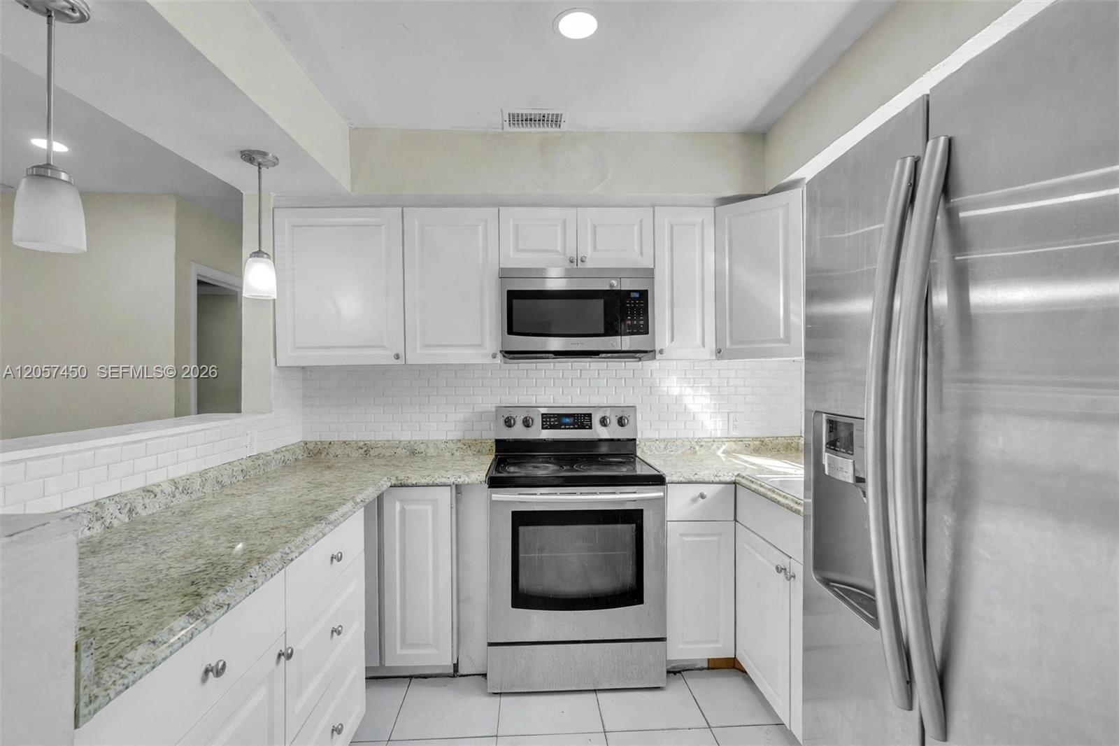 Kitchen featuring white cabinetry, stone-finish countertops, subway tile backsplash, stainless steel appliances, and pendant lighting