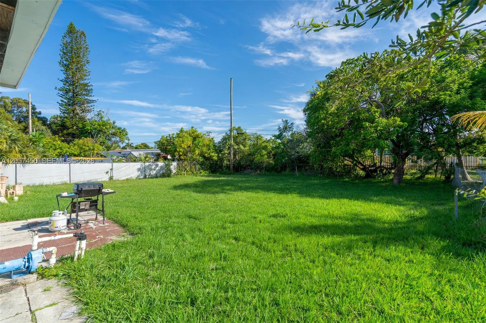 Expansive backyard featuring a large grass lawn, mature trees, and perimeter chain-link fencing