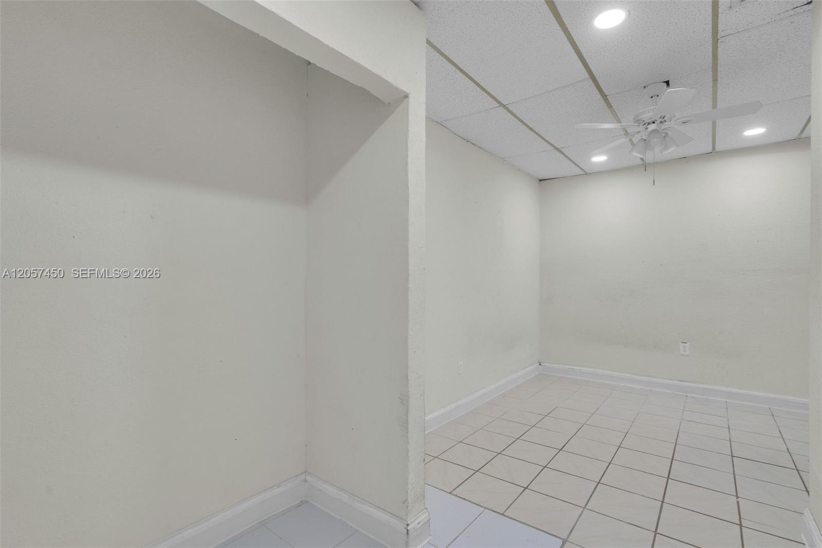 Interior space featuring neutral wall tones, white floor tiles, a drop ceiling with recessed lighting, and a white ceiling fan with integrated light fixtures