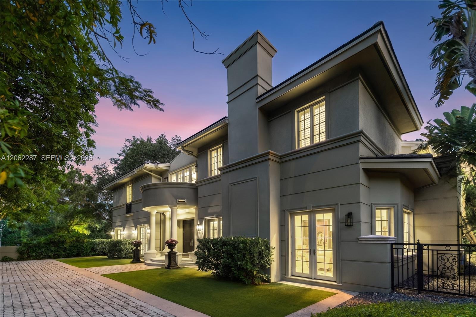 Two-story exterior featuring a stucco facade, a pillared entryway with a curved balcony, multi-pane windows, and a paved driveway