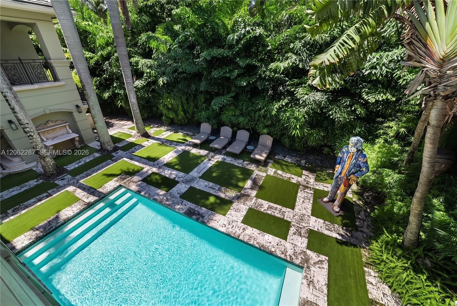 Swimming pool with concrete steps, integrated stone pavers, synthetic turf segments, and dense perimeter foliage