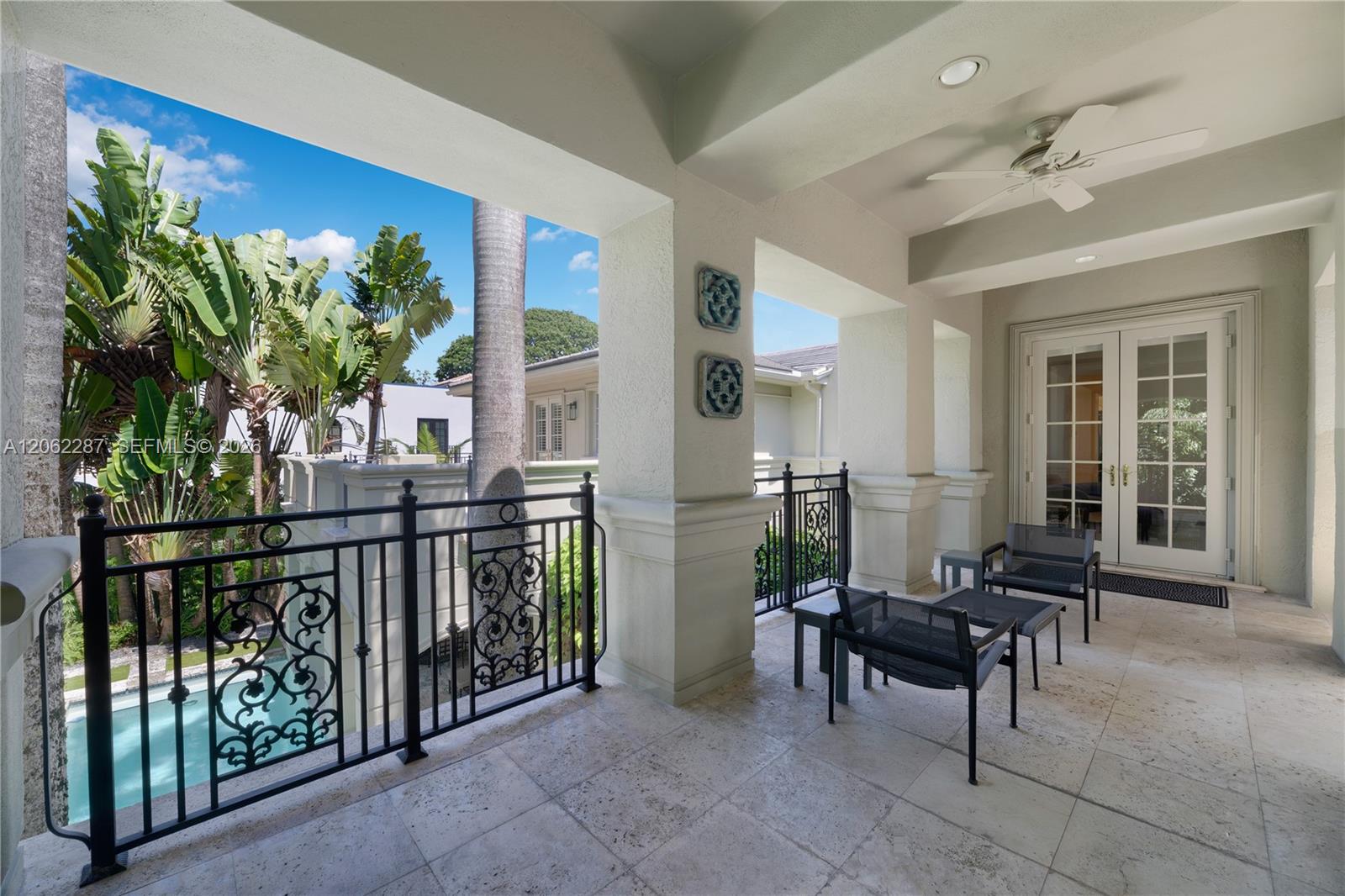Covered patio featuring stone tile flooring, decorative wrought iron railings, an integrated ceiling fan, and recessed lighting