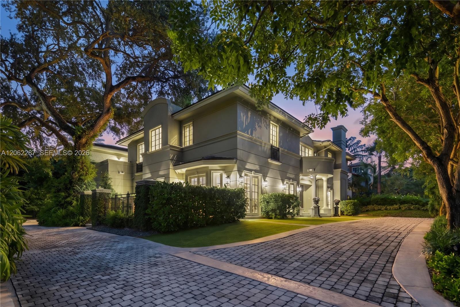 Two-story stucco exterior featuring architectural columns, multi-pane windows, arched entry, and a paver stone driveway