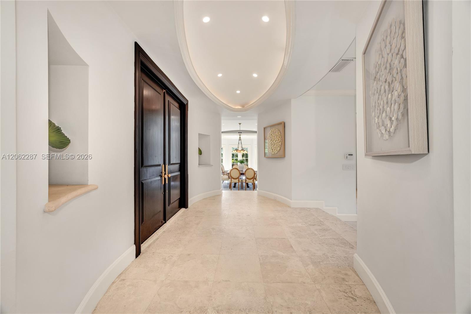 Foyer featuring stone tile flooring, double-door entry with brass hardware, oval tray ceiling with recessed lighting, and integrated wall niches