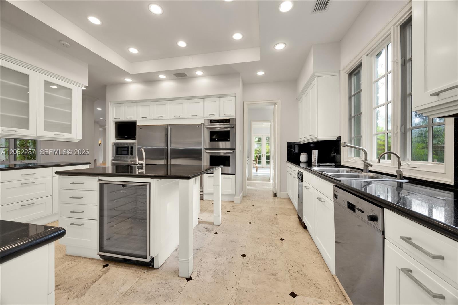 Kitchen featuring white cabinetry, dark stone countertops, stainless steel appliances, a central island with a built-in beverage refrigerator, and stone tile flooring with decorative inlay accents