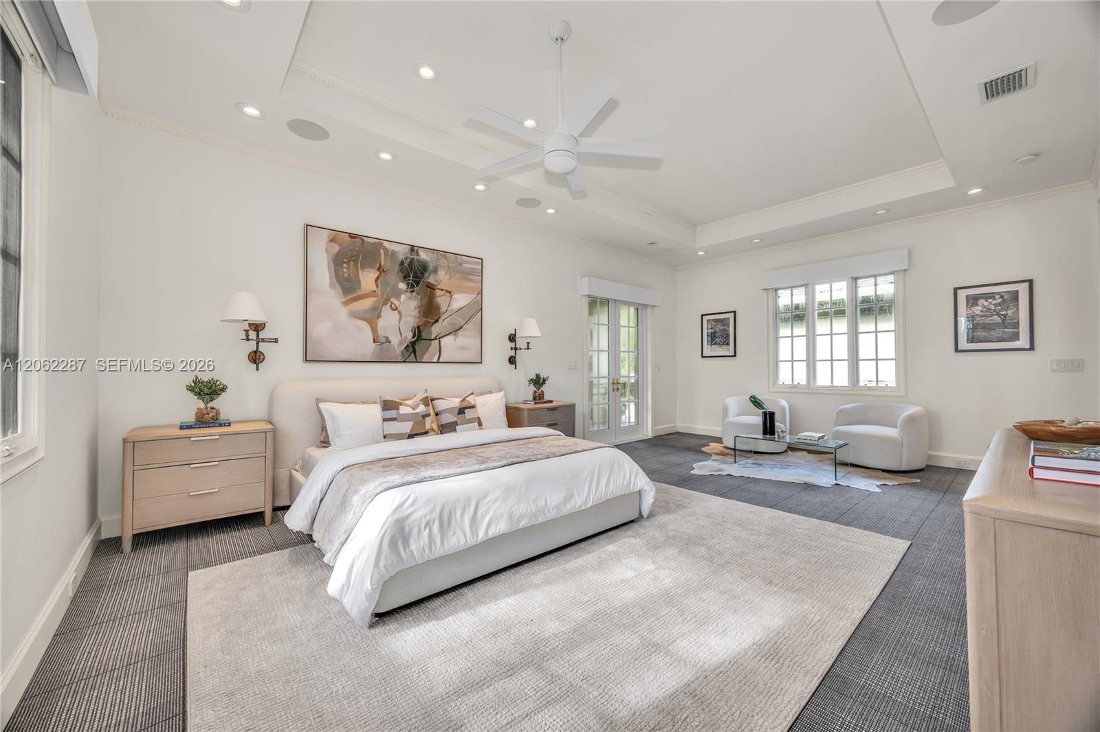 Spacious room featuring a recessed tray ceiling, white multi-blade ceiling fan, integrated recessed lighting, grid-pattern windows, and multi-light French doors