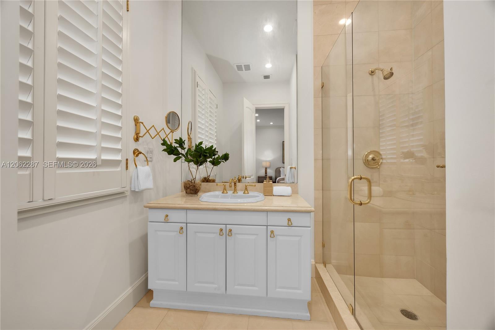 Bathroom featuring white cabinetry, stone-surface countertop, undermount sink, brass-finish fixtures, and a glass-enclosed shower with floor-to-ceiling tile