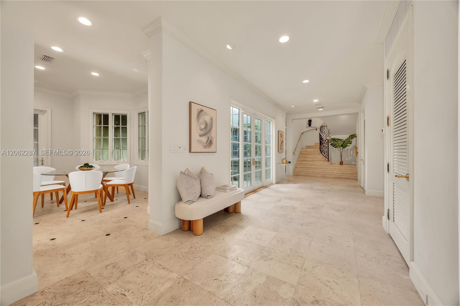 Open interior featuring large-format stone tile flooring, recessed lighting, double-paned glass French doors, and a staircase with a wrought-iron railing