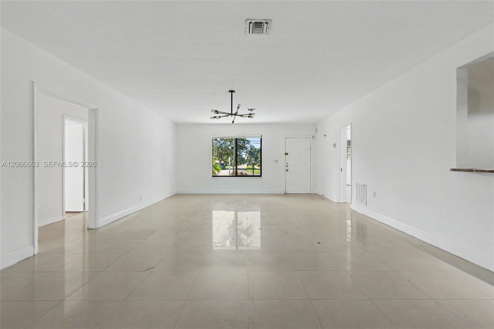 Open-concept interior featuring large-format tile flooring, neutral wall finishes, a multi-arm modern chandelier, and a prominent exterior window