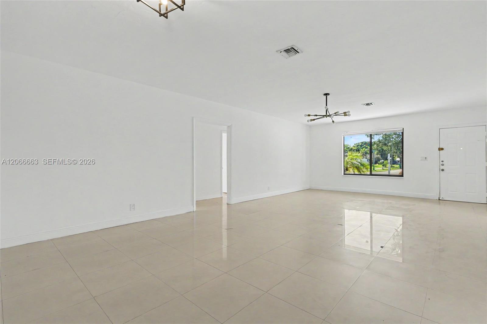 Open interior space featuring light-colored tile flooring, neutral wall finishes, a multi-arm modern light fixture, and large-paned window