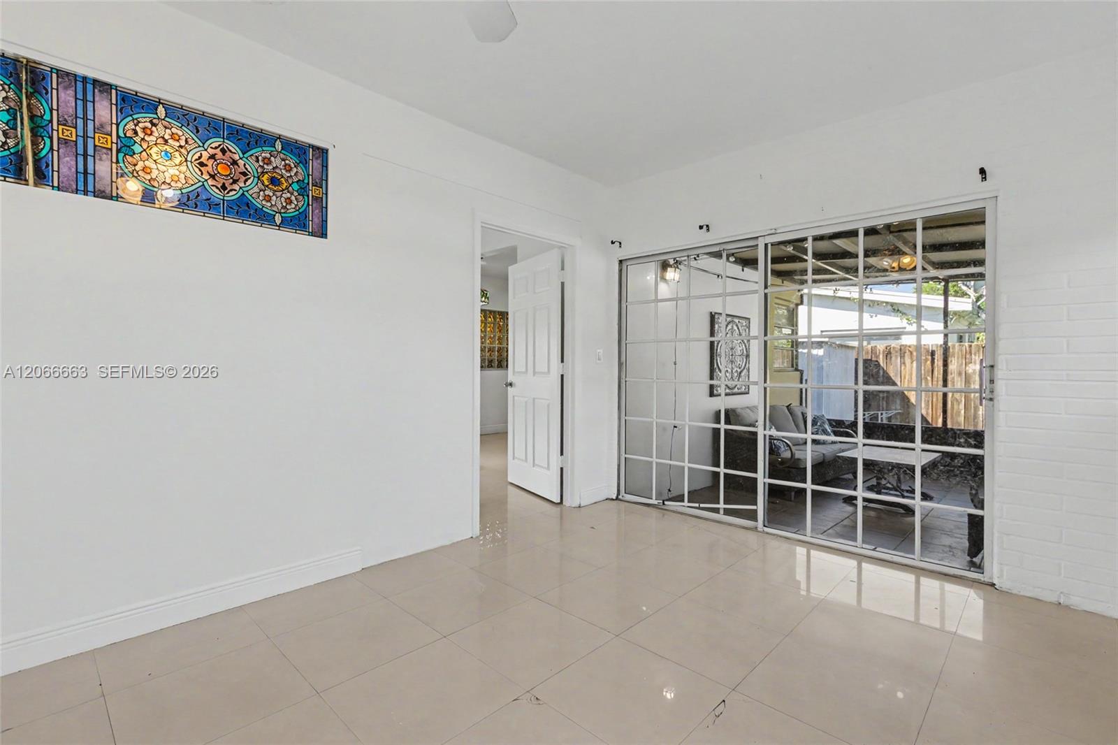 Interior space featuring large-format tile flooring, decorative stained-glass transom window, white-painted brick wall, and multi-pane sliding glass doors