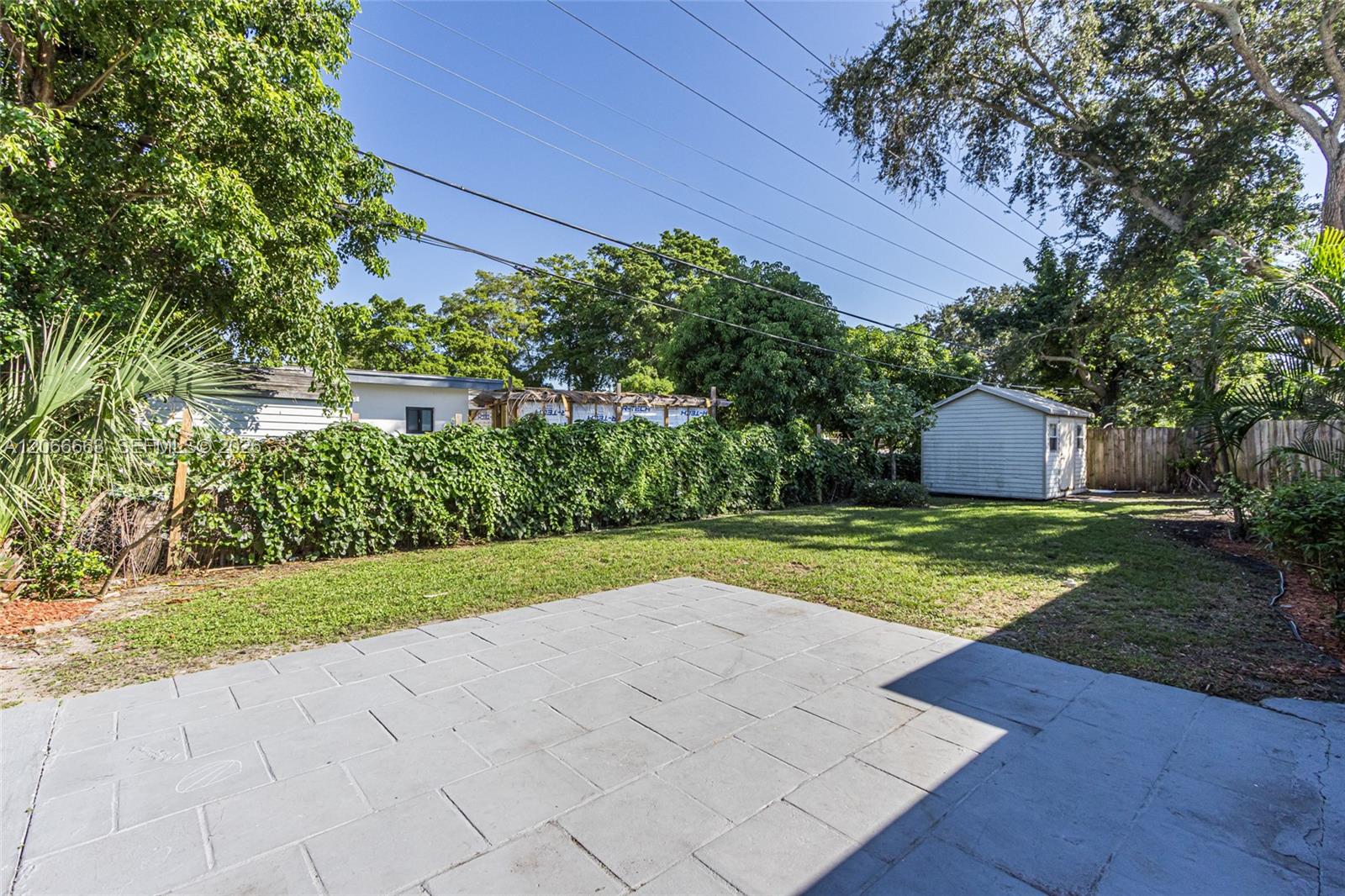 Backyard featuring a paved patio, grass lawn, detached storage shed, and mature trees