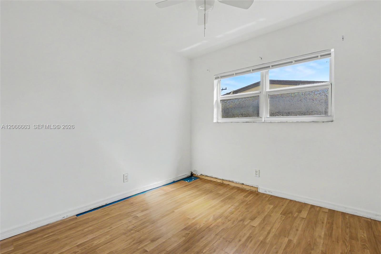 Interior room featuring wood-finish flooring, white walls, a horizontal sliding window, and a ceiling fan