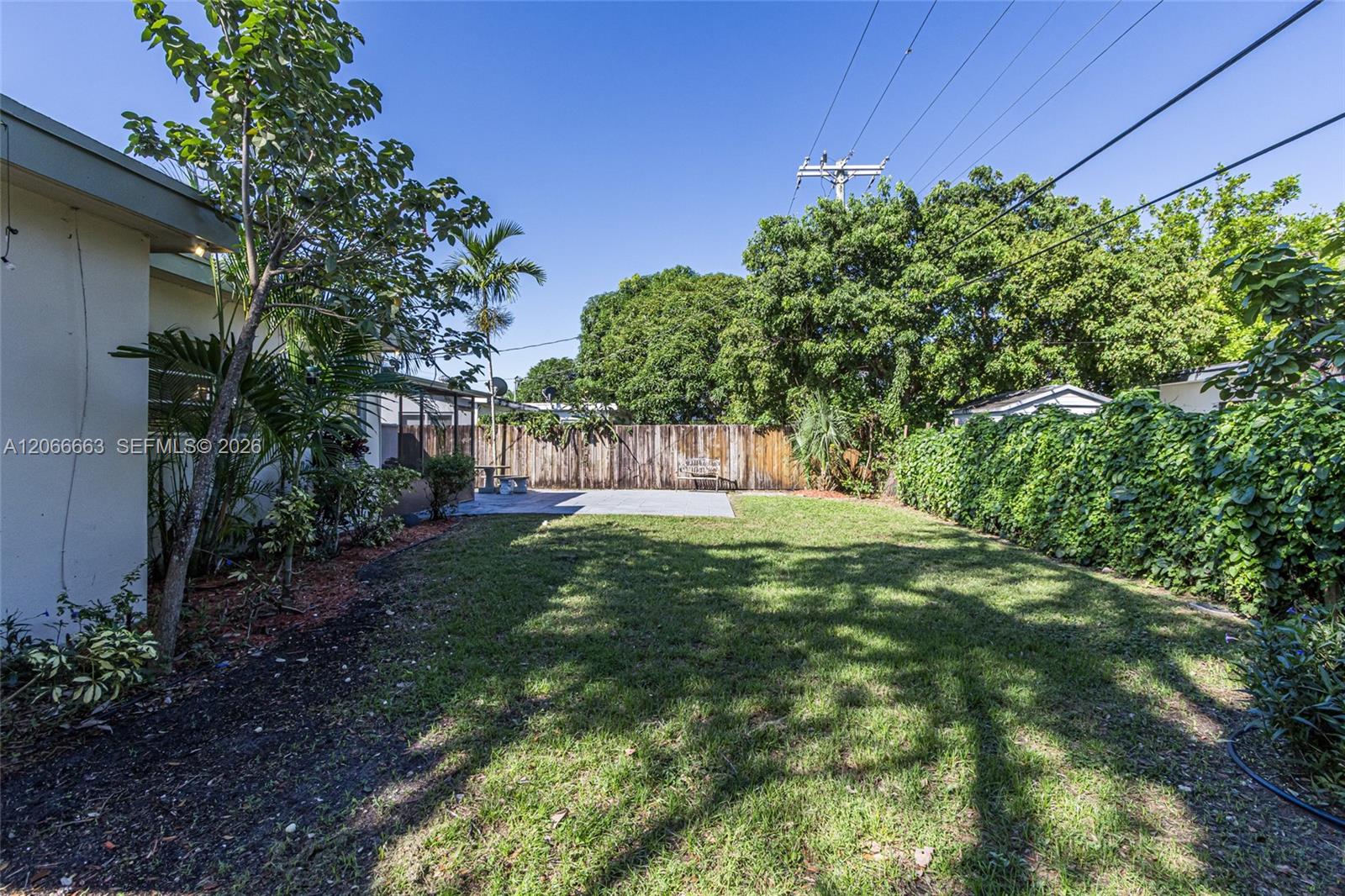 Expansive backyard featuring a manicured lawn, concrete patio, mature trees, and wooden perimeter fencing