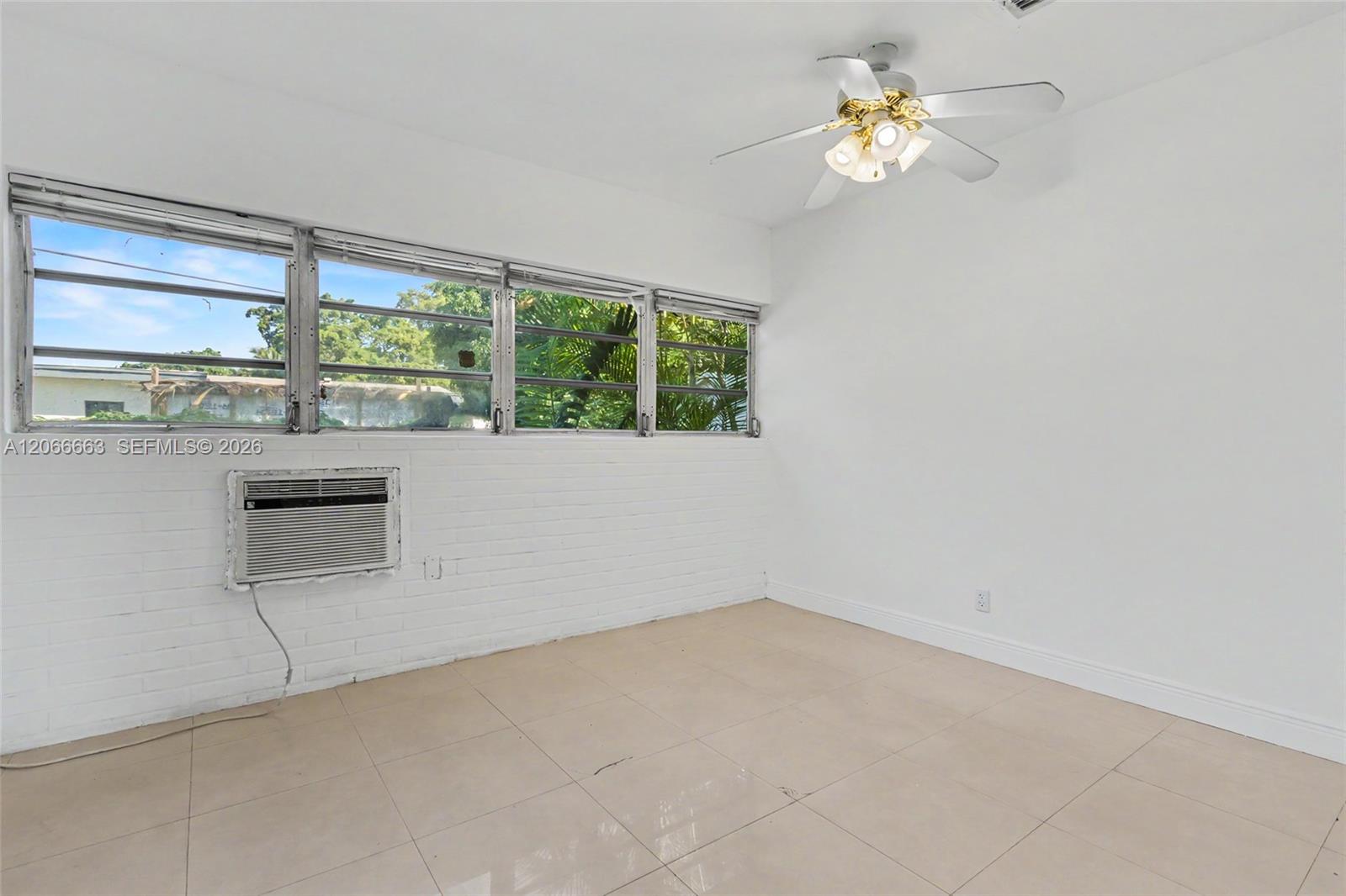 Room featuring white painted brick walls, neutral tile flooring, multi-pane casement windows, and a ceiling fan with integrated lighting