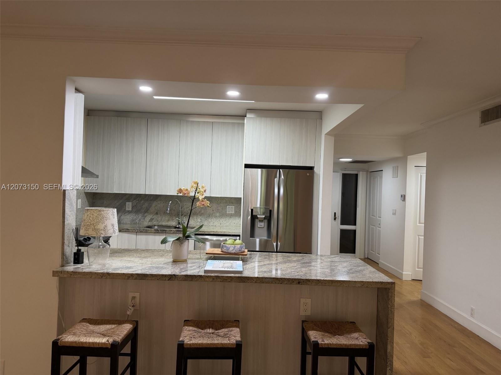 Kitchen featuring a stone-surface breakfast bar, light-tone cabinetry, recessed ceiling lighting, and stainless steel appliances