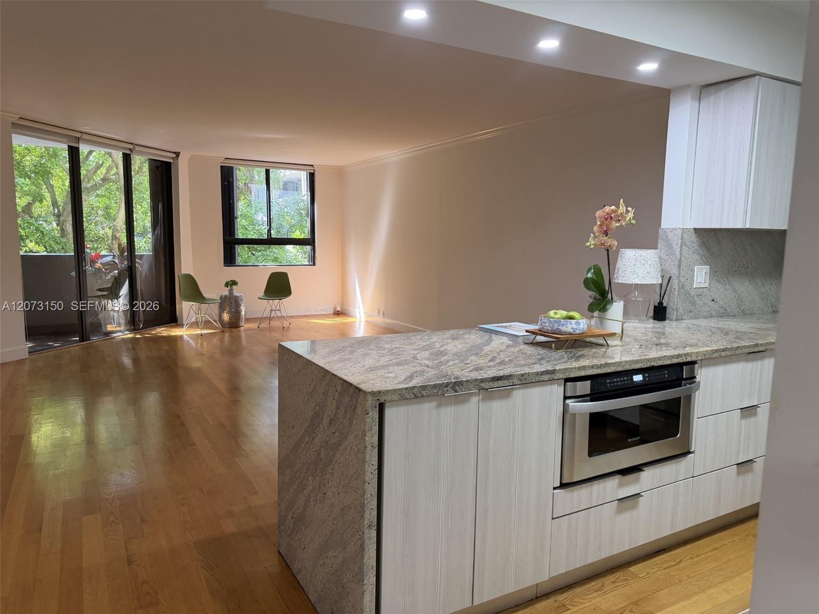 Kitchen featuring an island with stone-finish countertops and built-in microwave, light-toned cabinetry, recessed lighting, and wood-finish flooring throughout