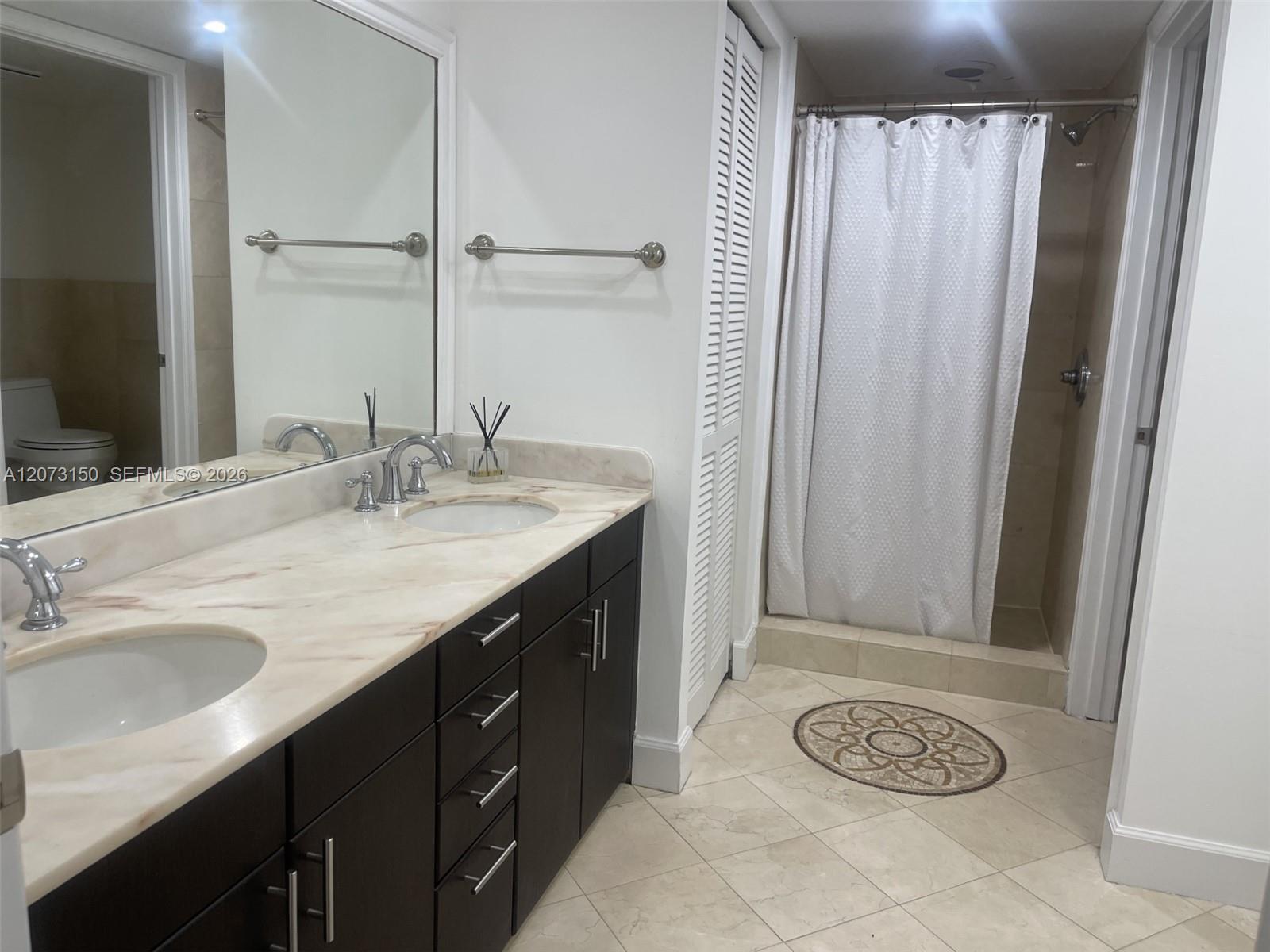 Bathroom featuring a dark wood vanity with dual under-mount sinks, a stone countertop, oversized wall mirror, and a walk-in shower with tile flooring