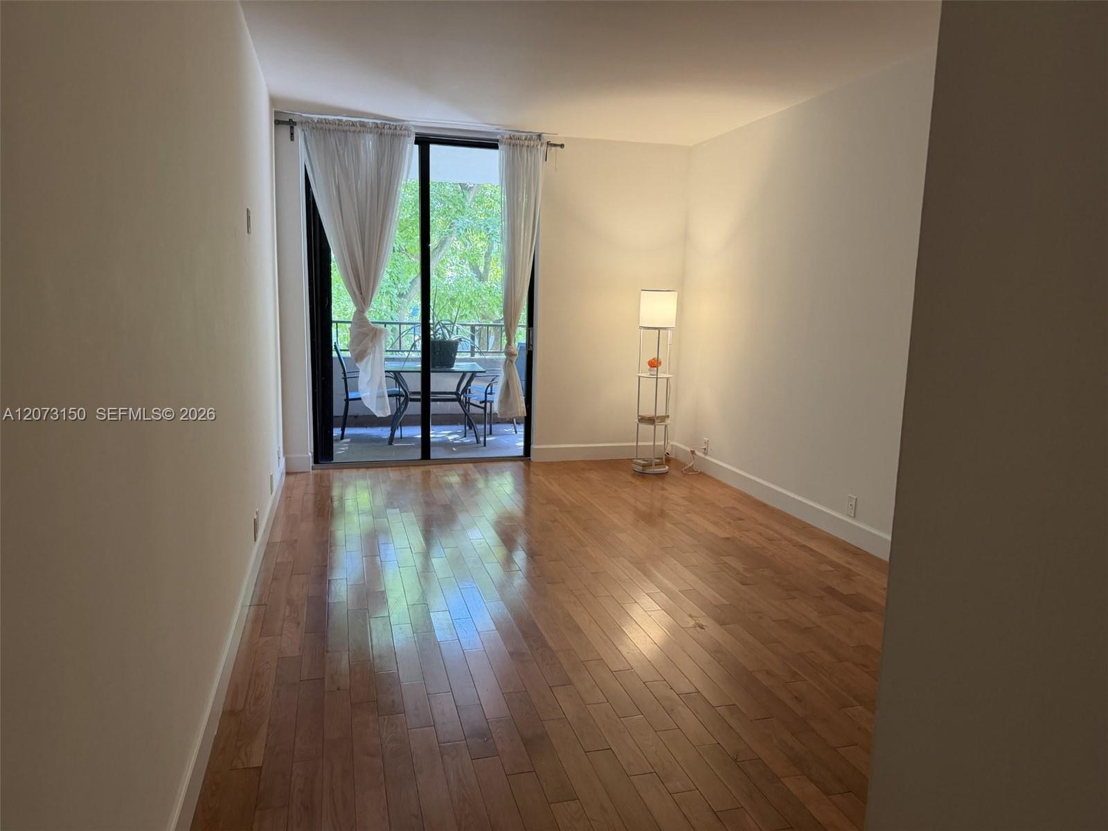 Living area featuring wood-finish flooring and floor-to-ceiling glass sliding doors opening to a balcony