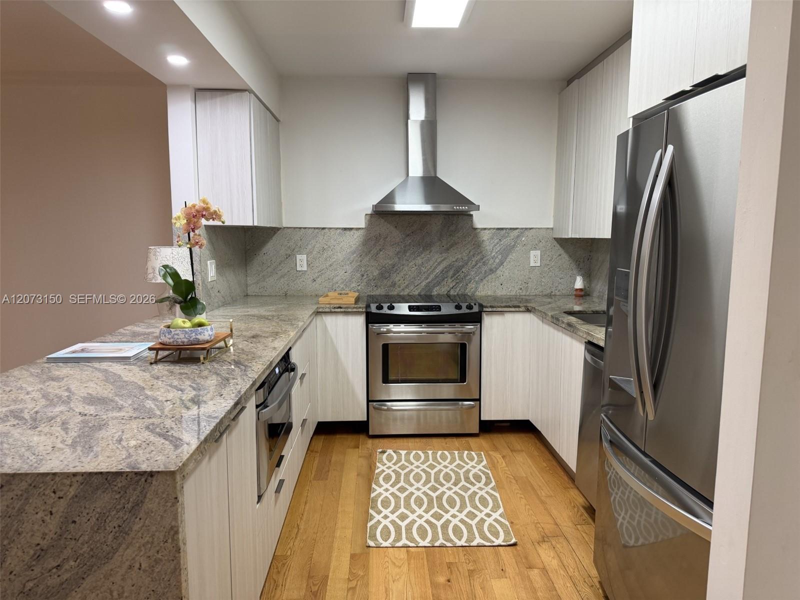 Kitchen featuring stone countertops, white vertical-grain cabinetry, stainless steel appliances, a chimney-style range hood, and wood-finish flooring