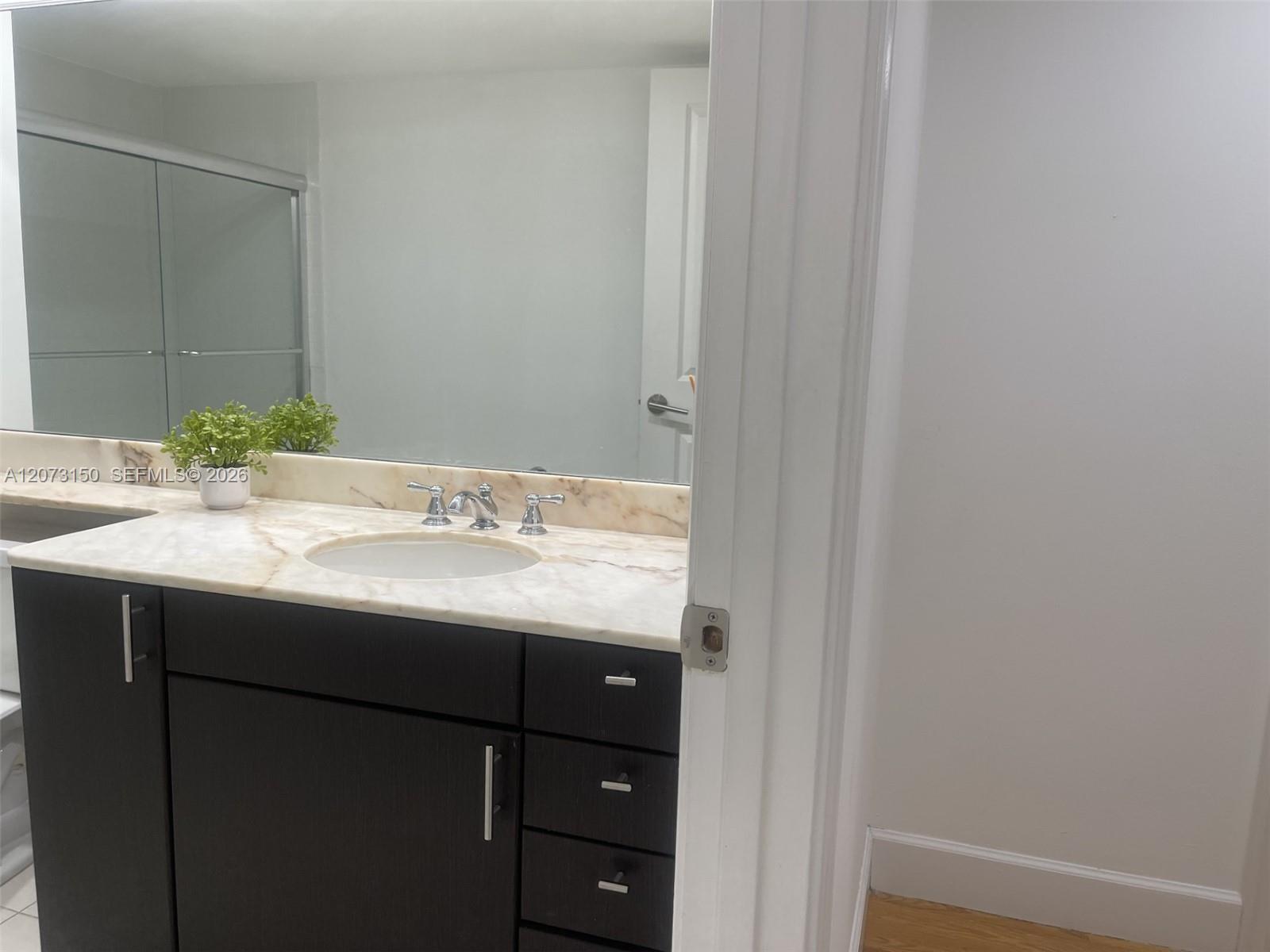 Dark cabinetry with silver-tone hardware, stone-surface countertop, integrated basin, widespread chrome faucet, and expansive wall-mounted mirror