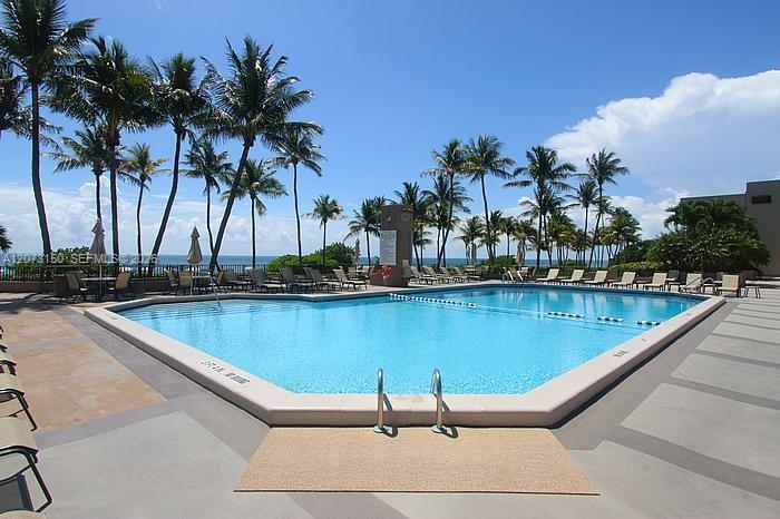 In-ground swimming pool featuring a concrete deck, metal handrails, and mature palm trees